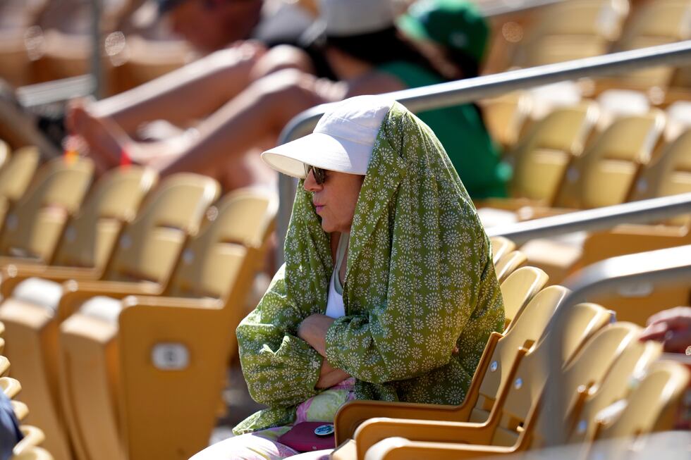 ARCHIVO – Una aficionada al béisbol se cubre del sol durante la cuarta entrada de un partido...