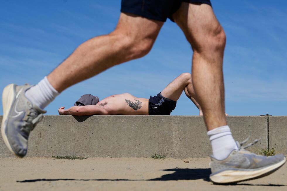 ARCHIVO - Un corredor pasa mientras un hombre toma el sol en un día caluroso en Crissy Field,...